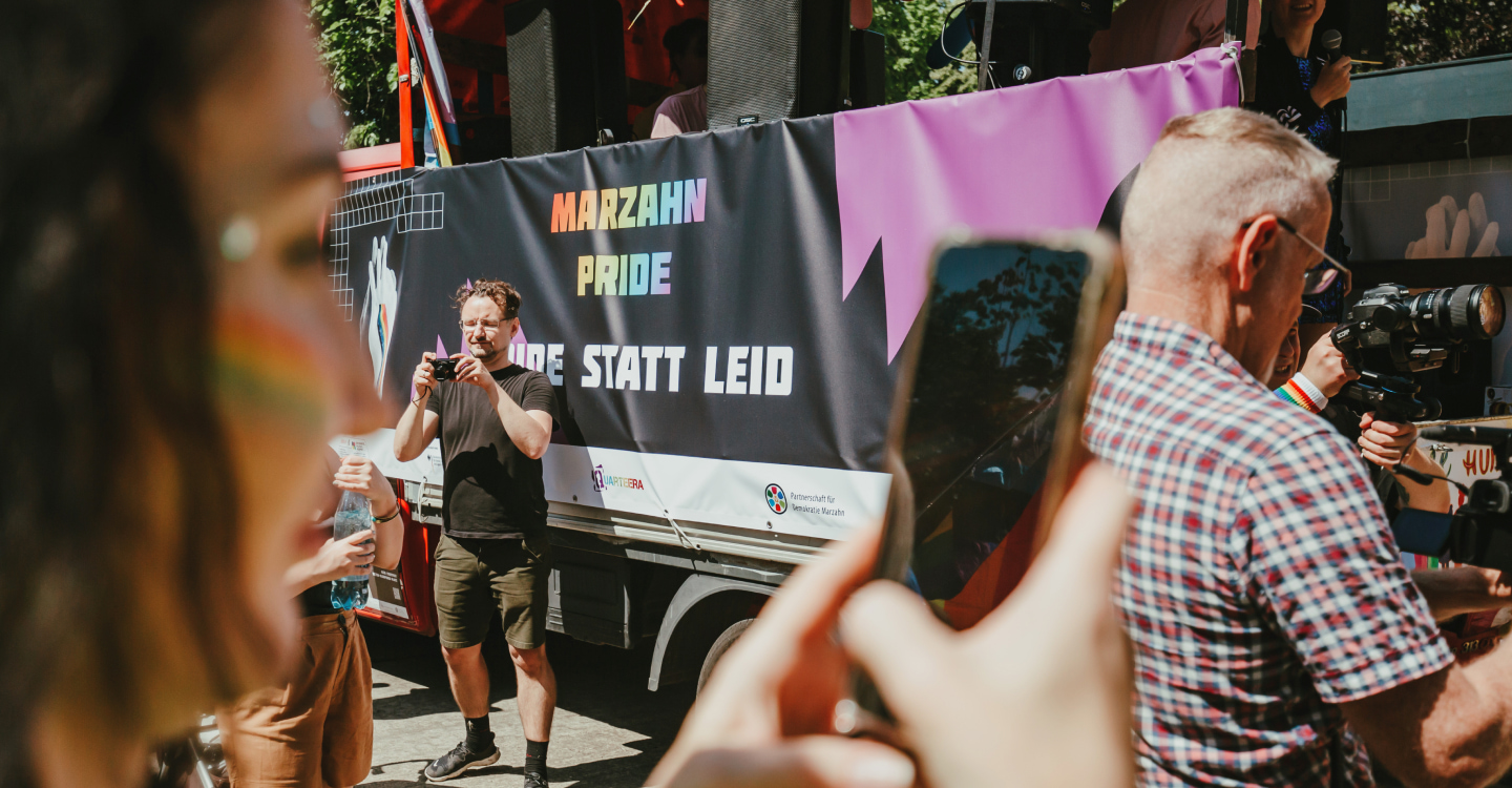 Marzahn pride truck with a banner with a 3 people in front of it